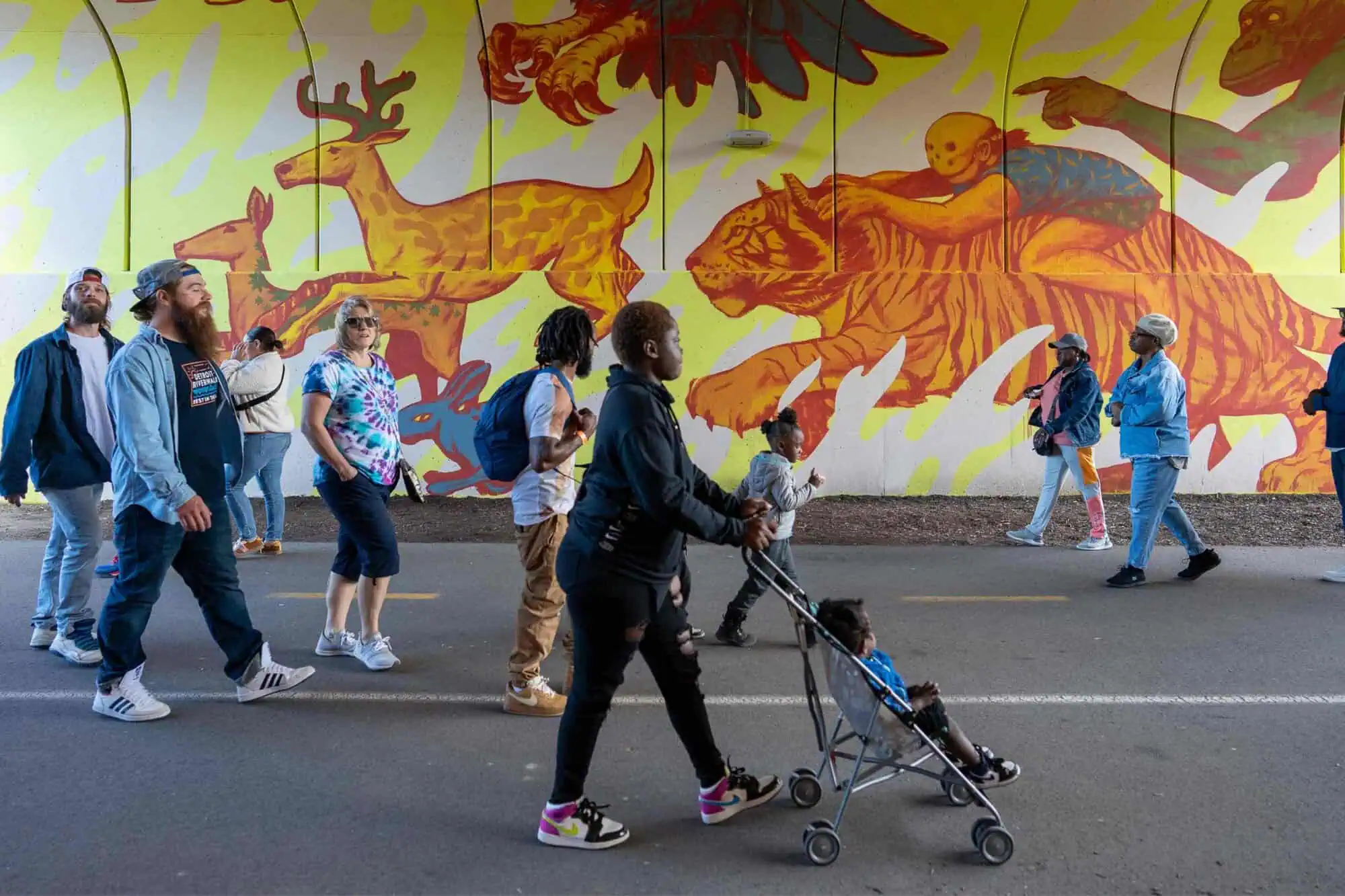 People walking both directions through a tunnel with murals on the rounded walls.